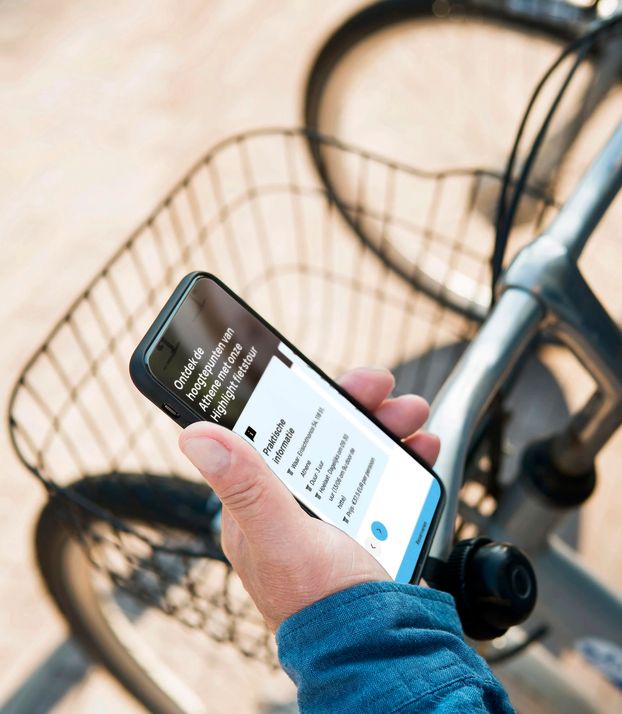 Iemand op de fiets houdt een smartphone vast die de website van Meet in Athens bekijkt.