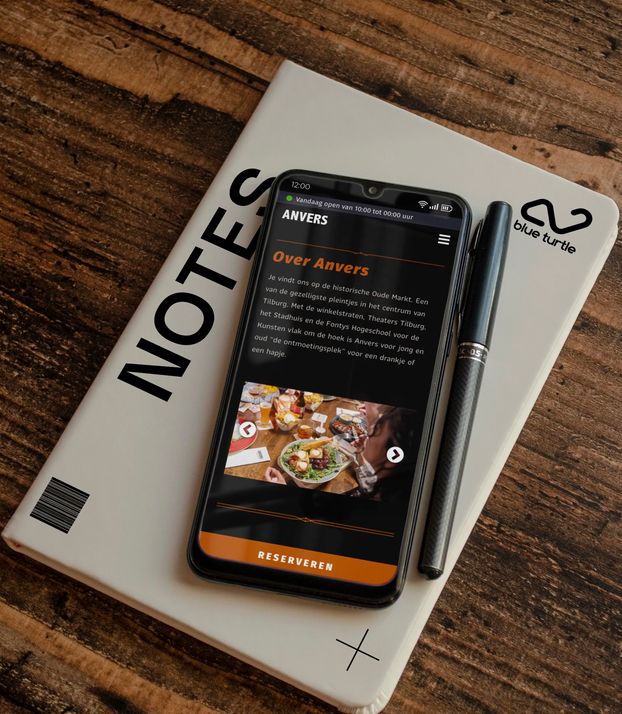 Een smartphone ligt op een tafel met daarop het gedeelte van de website: 'Over Anvers'.